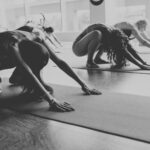 Kobiety ćwiczą joge na matach po środku sali.